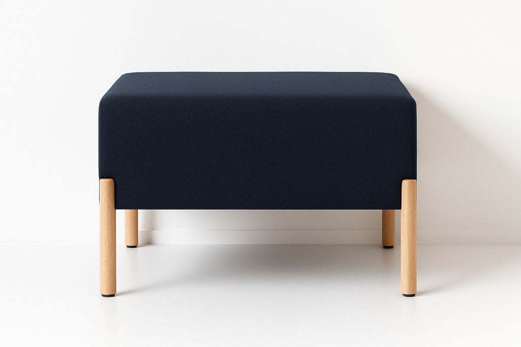 Porventura COD ottoman, upholstered in black Camira fabric with beech wood legs, combining a cushioned square form with an understated contemporary design.