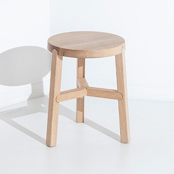 O banco Porventura Glyph apresenta um design elegante, com assento redondo e pés em metal, ideal para espaços interiores modernos.